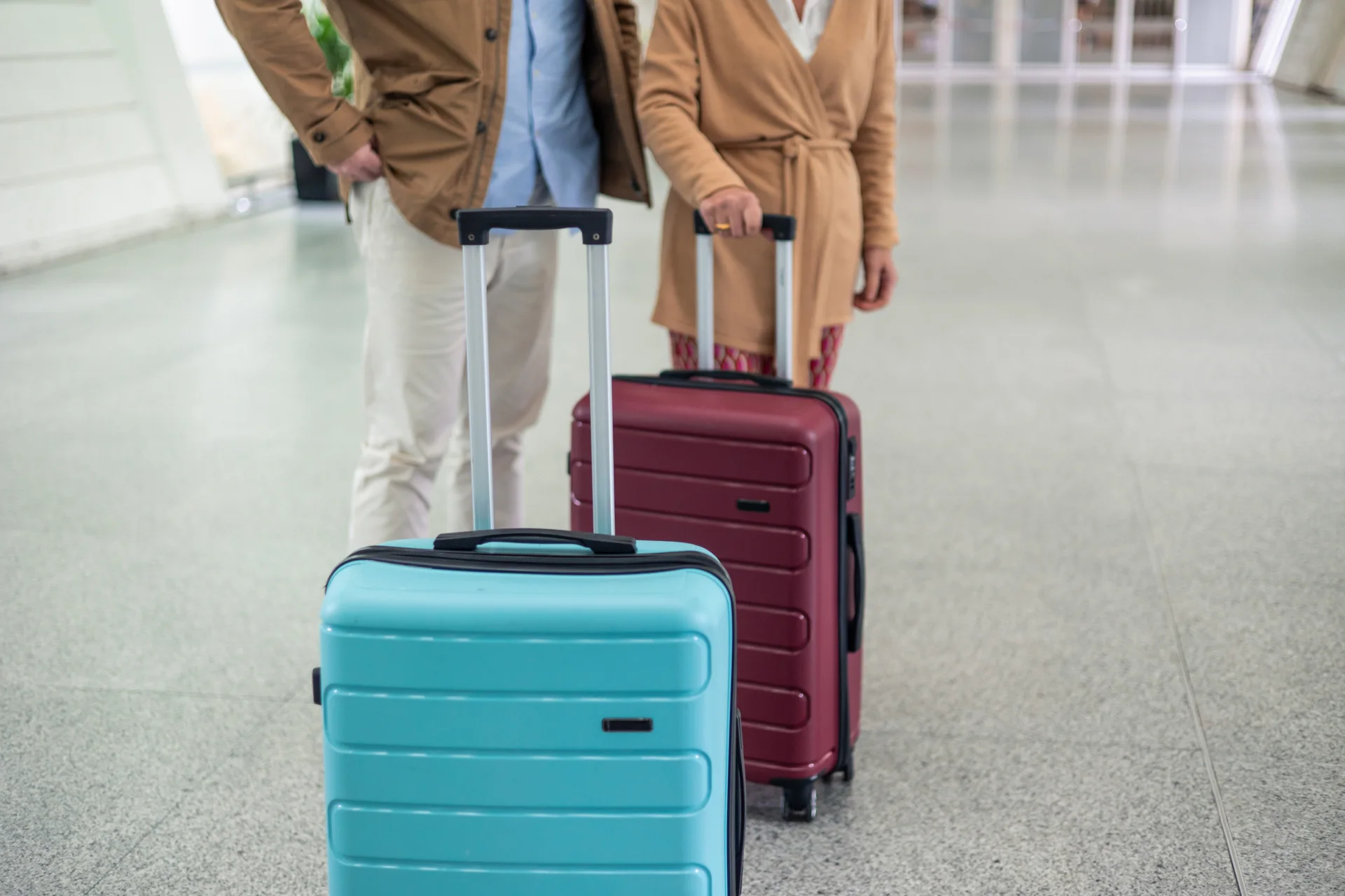 Two travellers holding wheeled suitcases in an indoor concourse